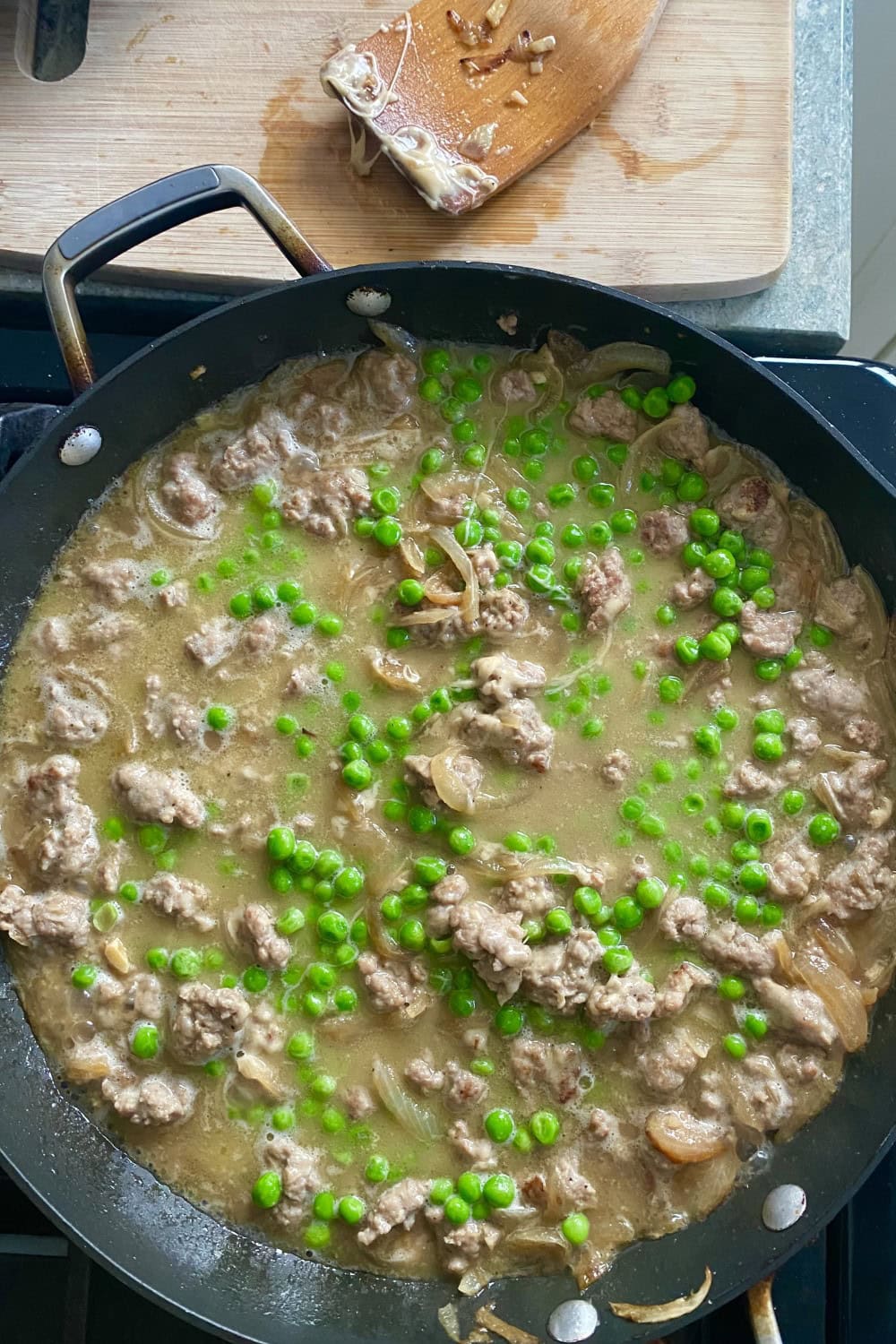 A sauté pan with peas, sausage and onion sauce on the stovetop.