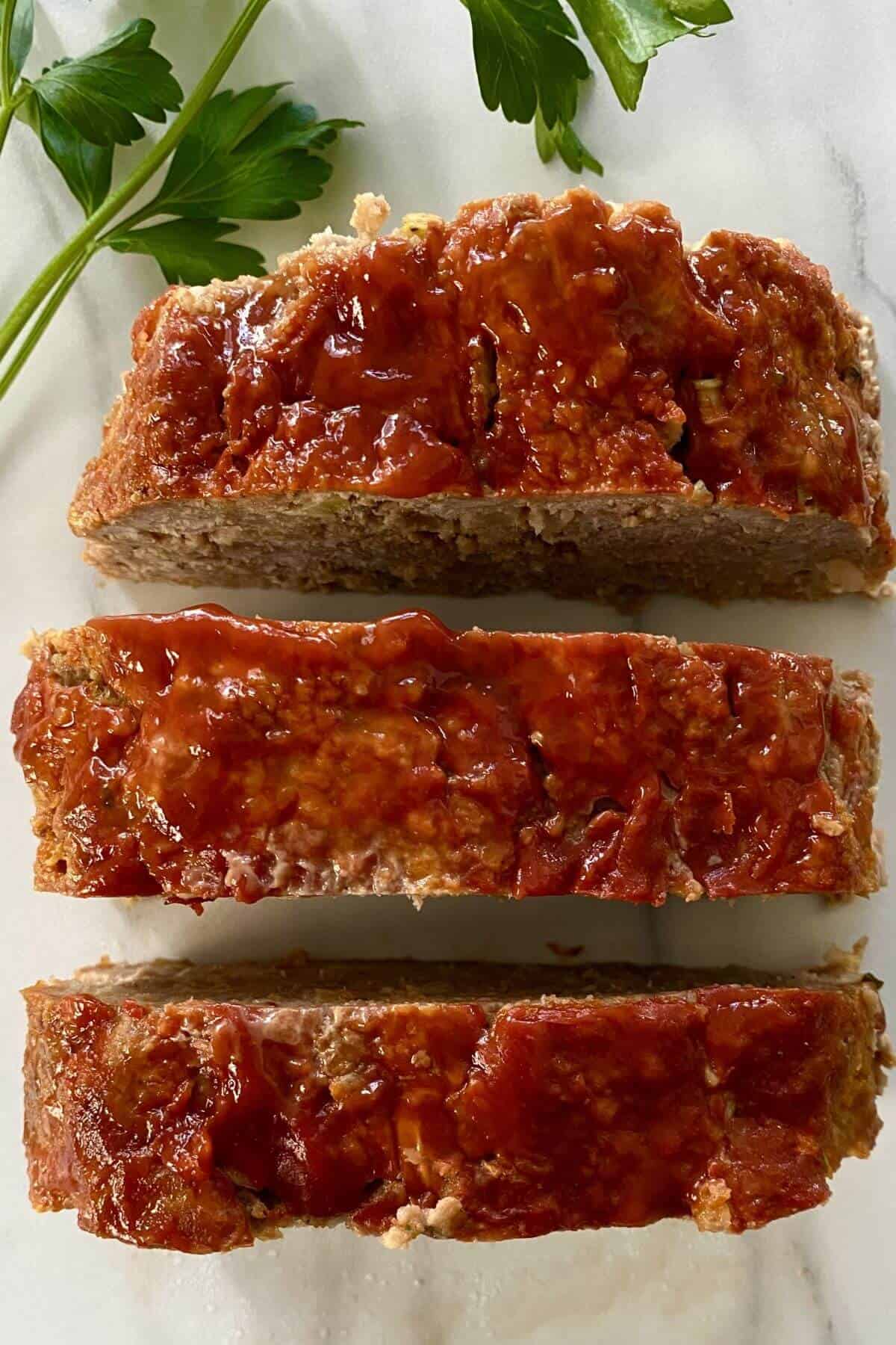 3 slices of meatloaf topped with ketchup.