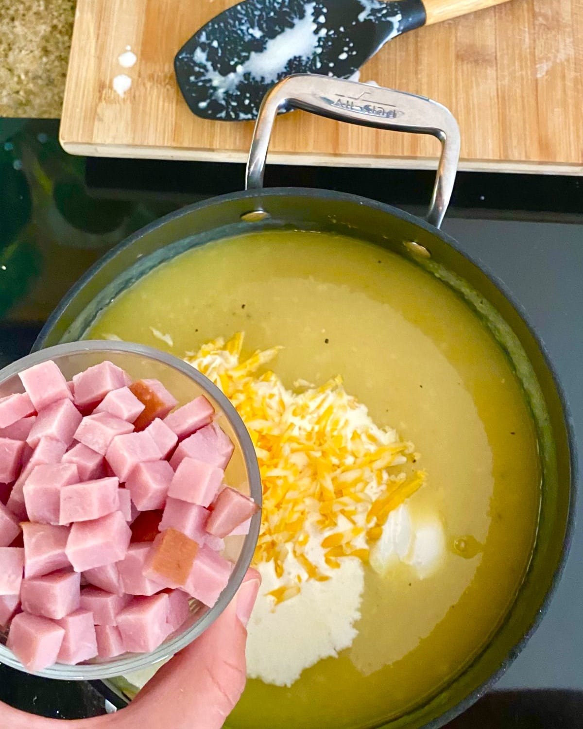 adding cheese, sour cream and ham to chowder.