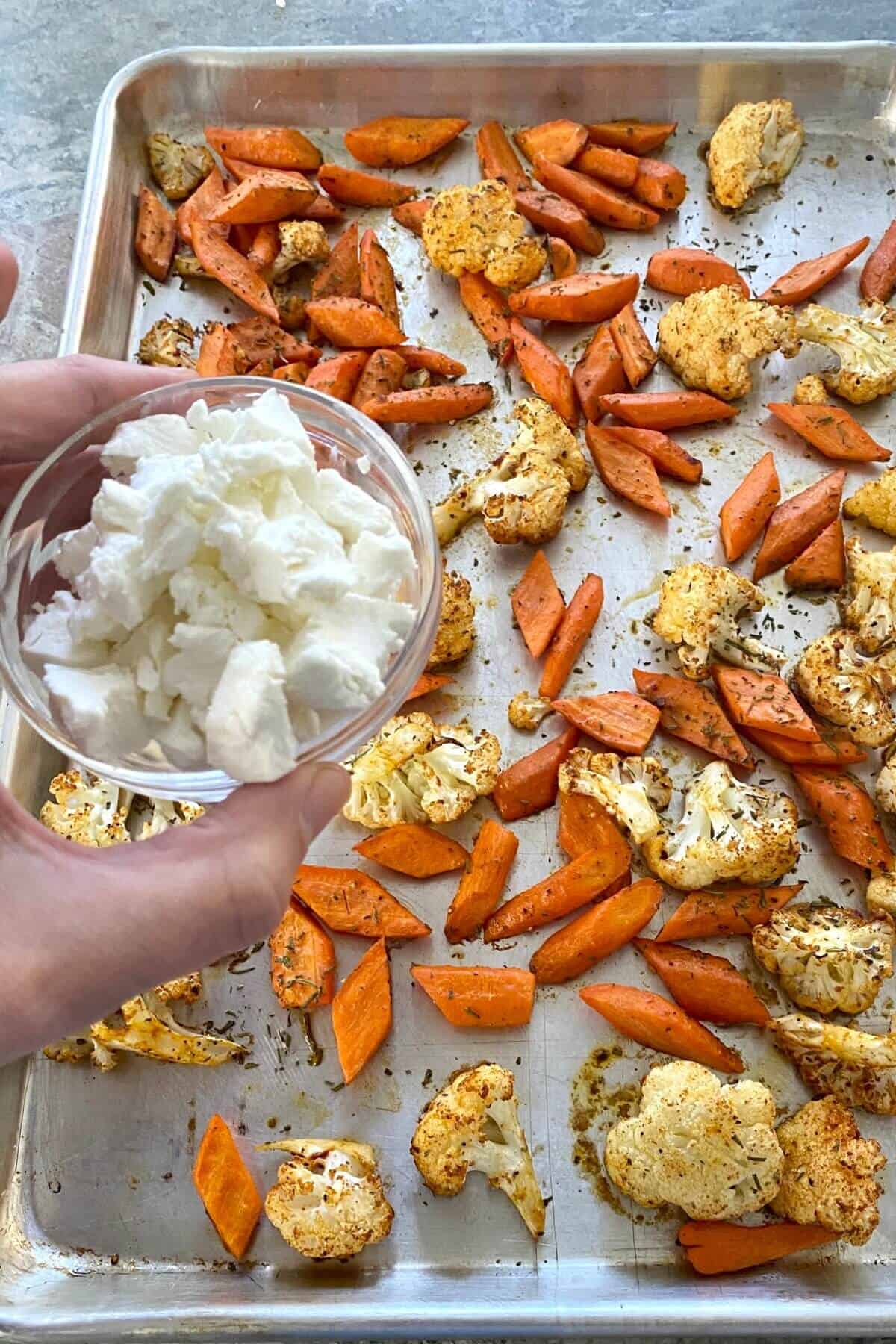 adding goat cheese to roasted carrots and cauliflower.
