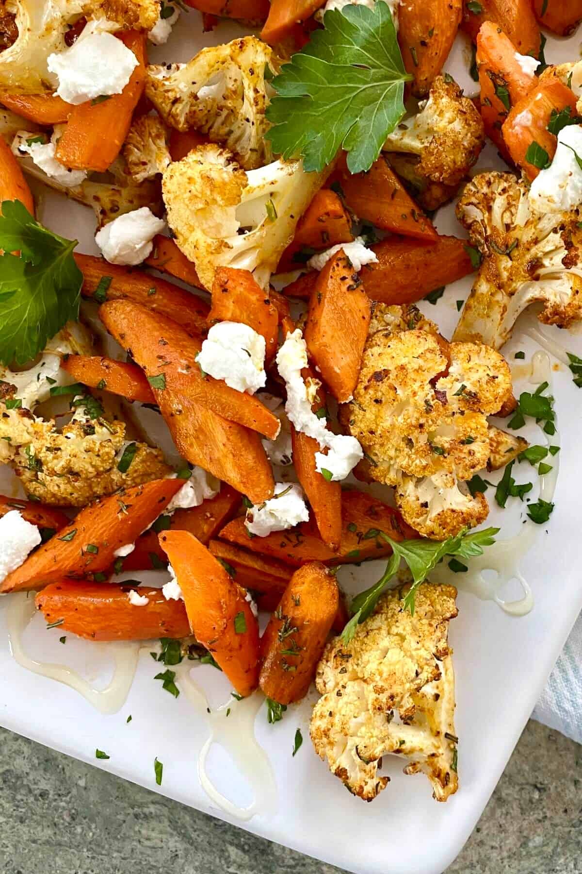 roasted carrots and cauliflower with goat cheese on a white platter.