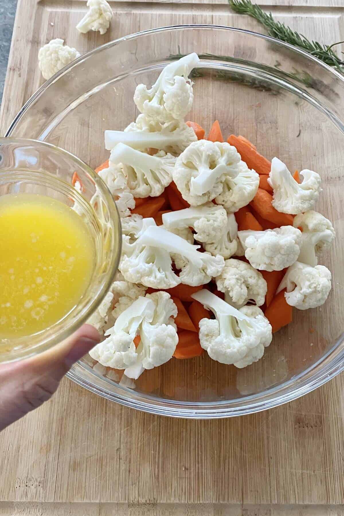 adding melted butter to vegetables in a bowl.