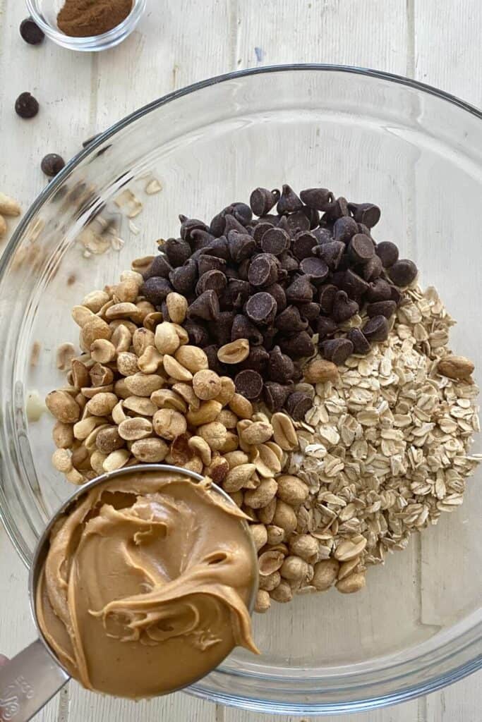 adding peanut butter to oats, peanuts and chocolate chips for oat bars.