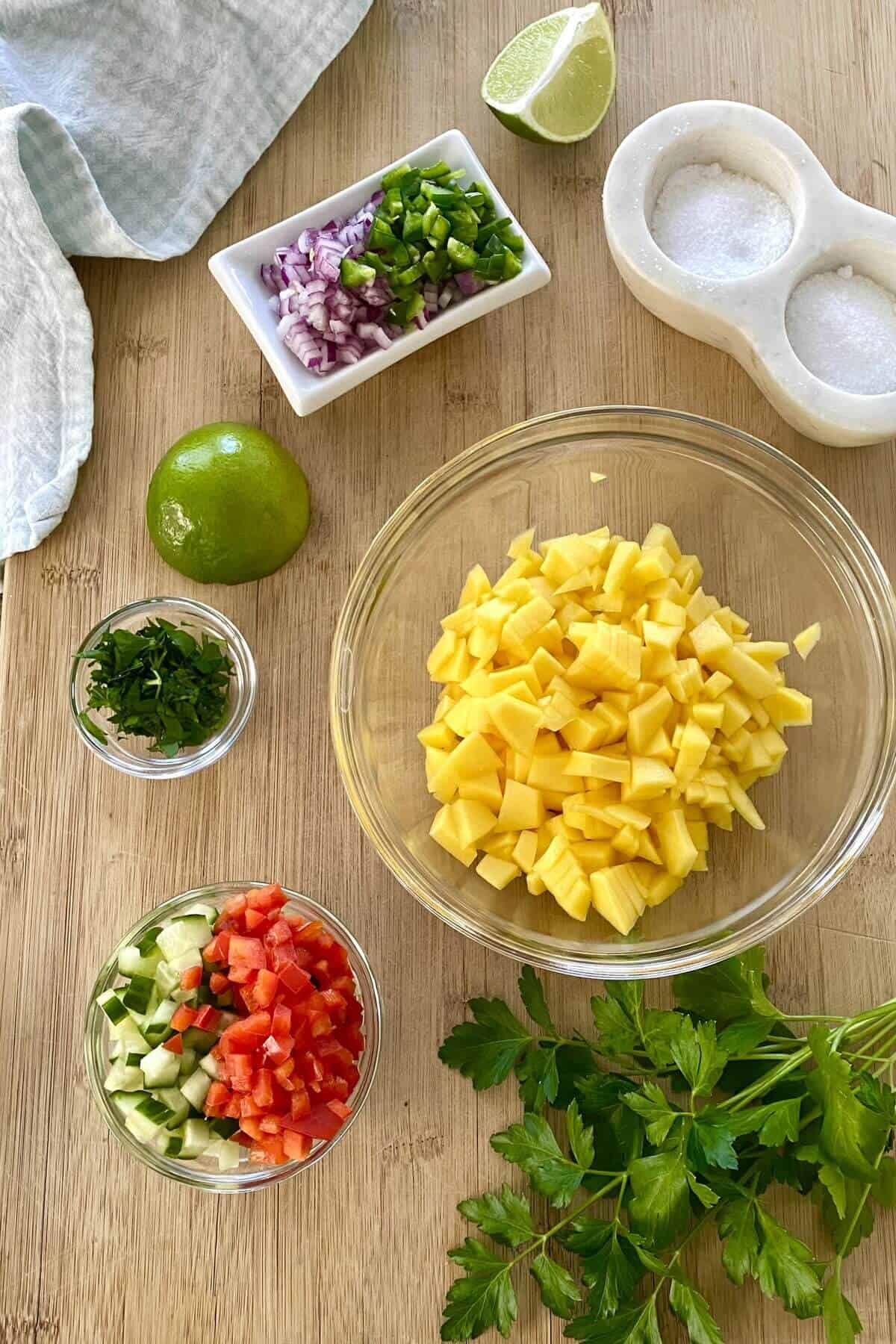 Mango, chopped red pepper, jalapeno, lime on a cutting board.