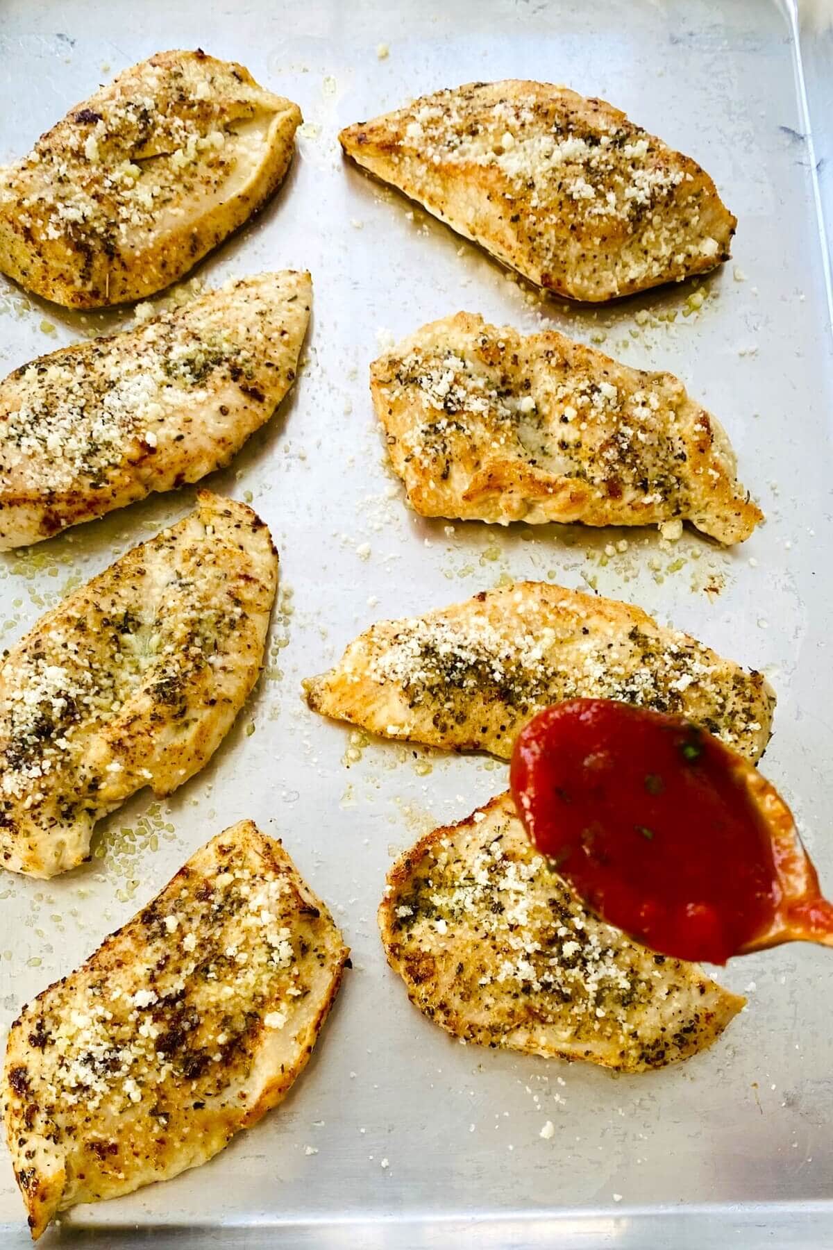 adding marinara to cooked chicken for parmesan.