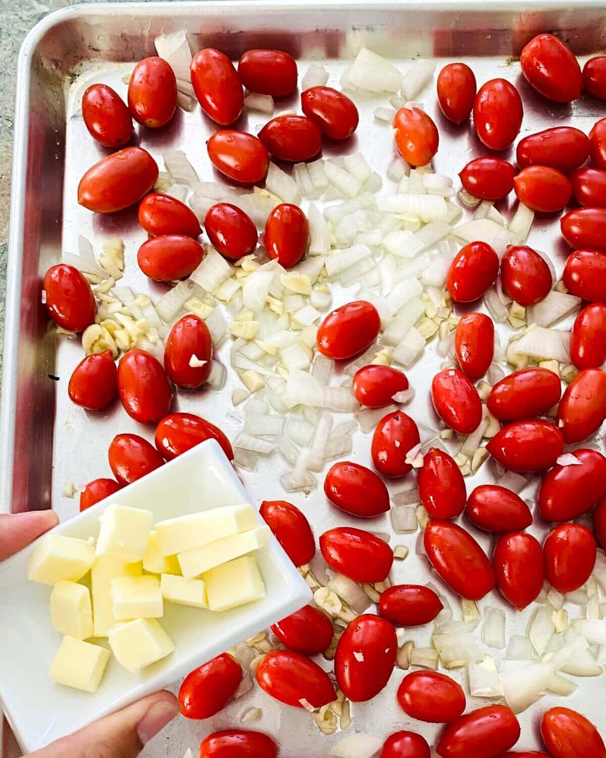 adding salted butter to baking sheet with cherry tomatoes.