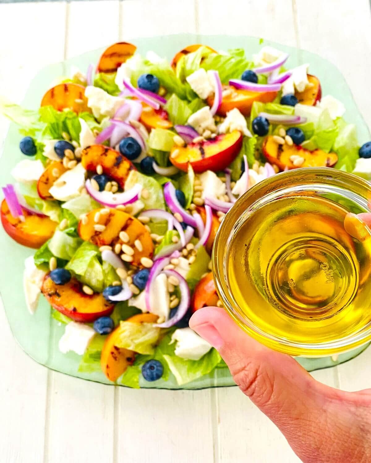 Adding olive oil to a salad with grilled peaches.