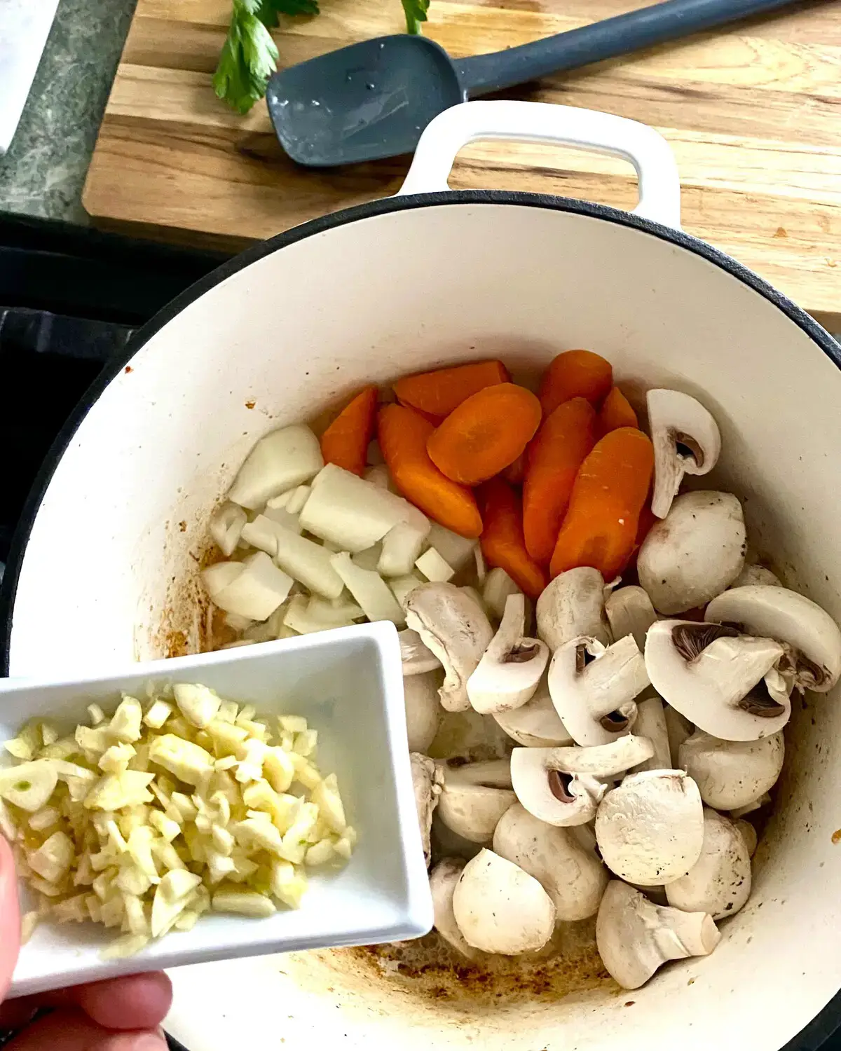 A dish of chopped garlic and a pot with sliced onion, mushrooms and carrots.