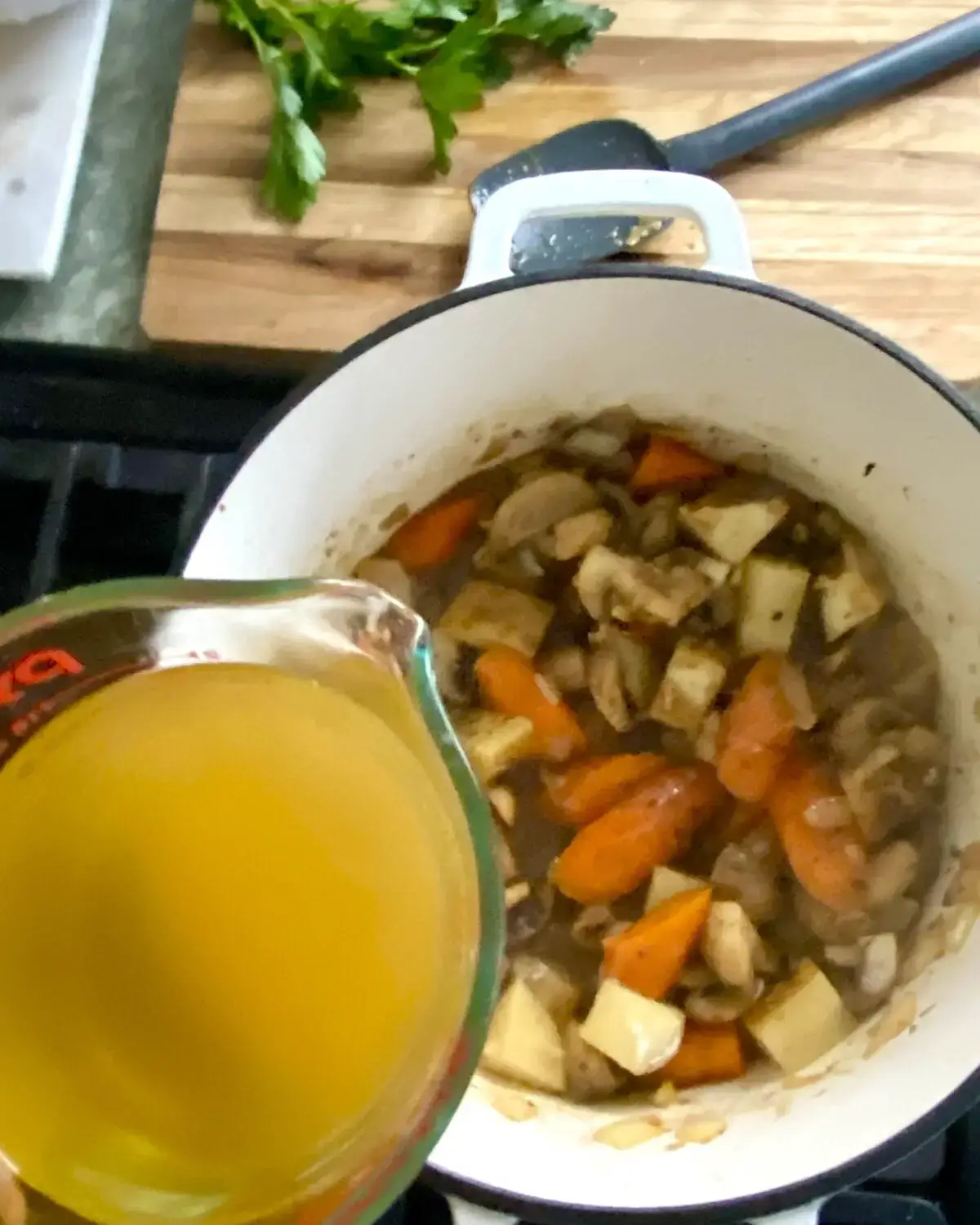 Adding chicken stock to pork stew.