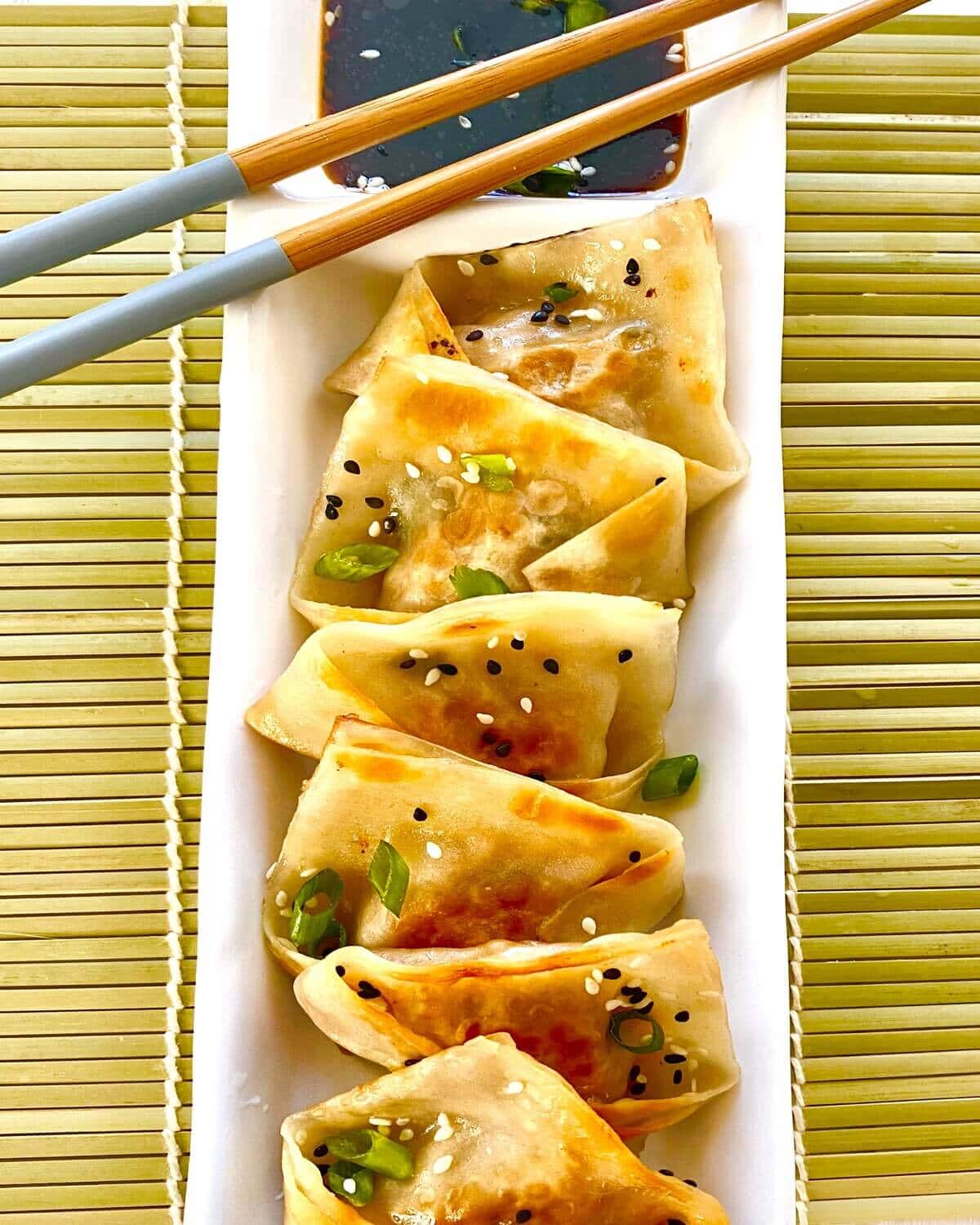 Pork potstickers on a plate with chopsticks.