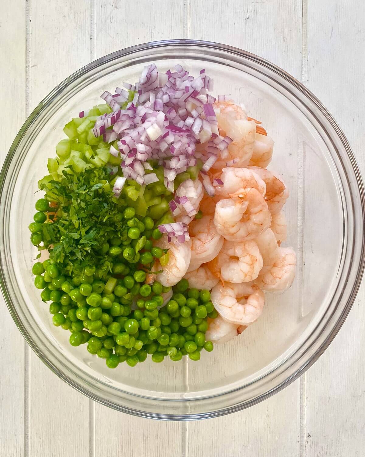 cooked shrimp, chopped celery, red onions and parsley in a glass bowl.