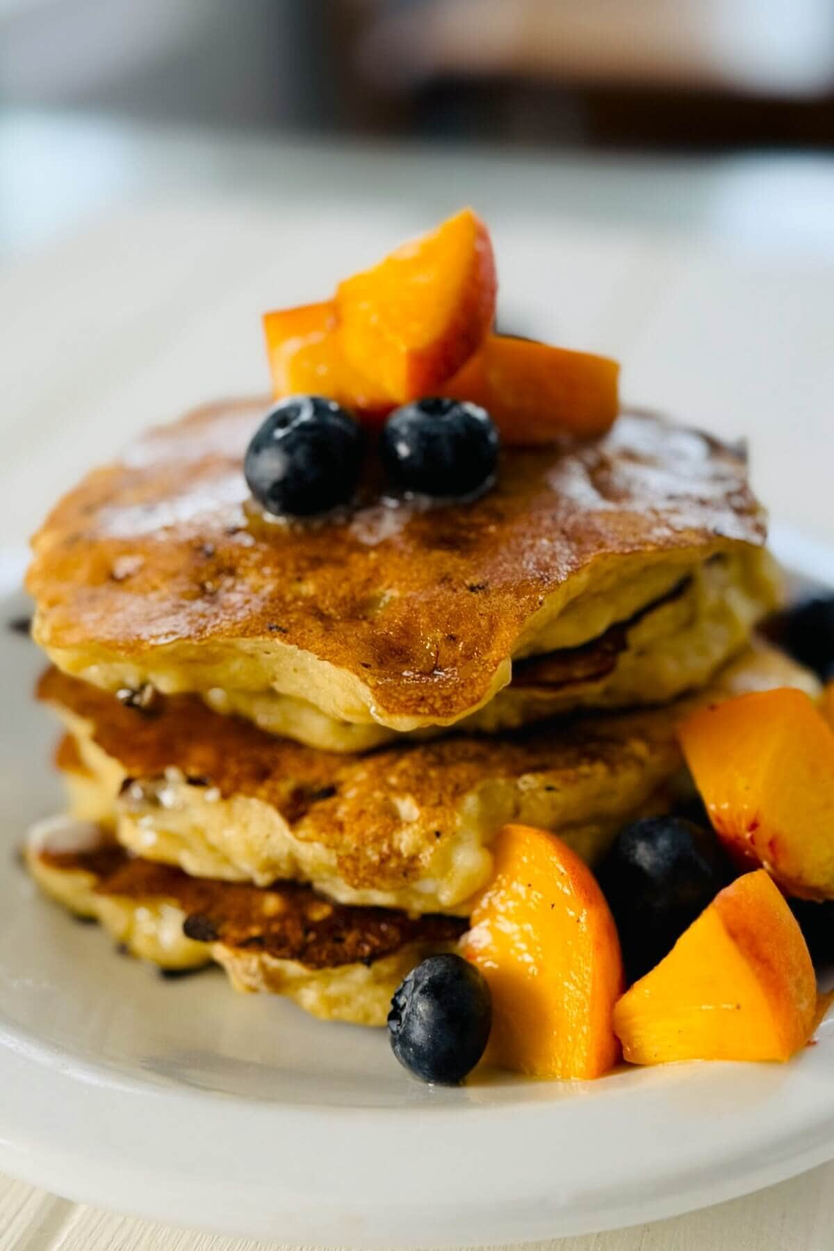 Stack of 3 protein pancakes with bananas with peaches and blueberries.