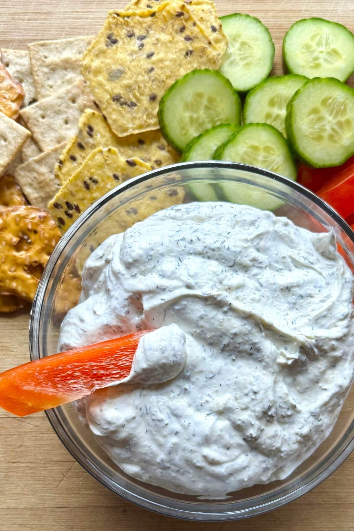 A bowl of dill dip with a bell pepper dipped in it.