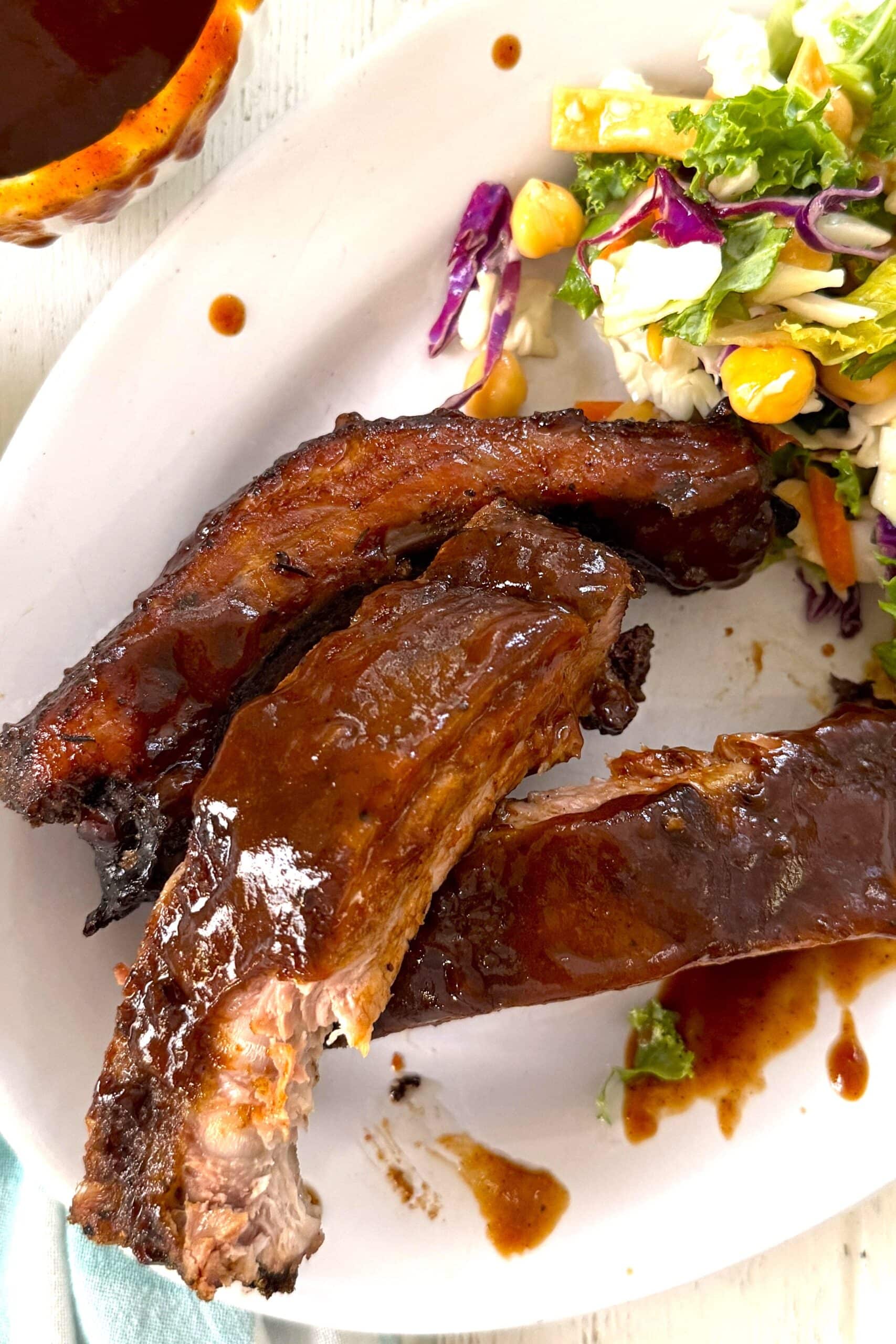 3 baked baby back ribs on a plate with salad.