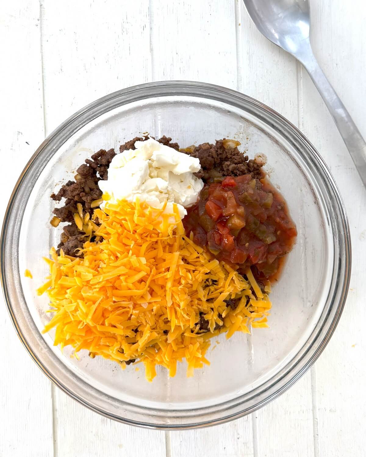 Cooked ground beef, shredded cheese, salsa, and cream cheese in a bowl.
