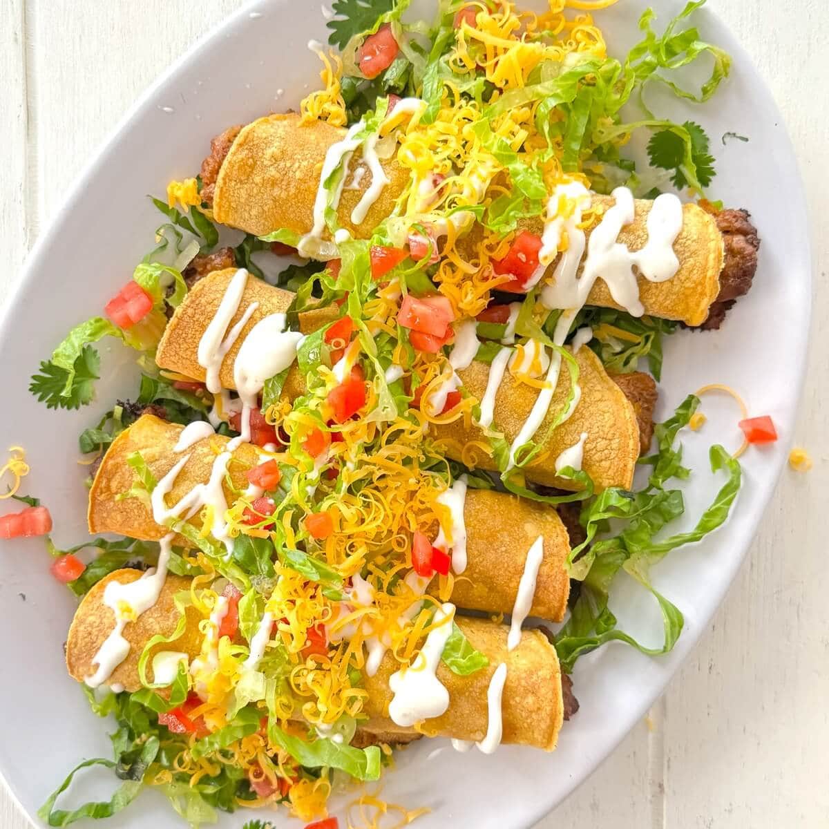 Rolled beef and cheese taquitos on a white plate.