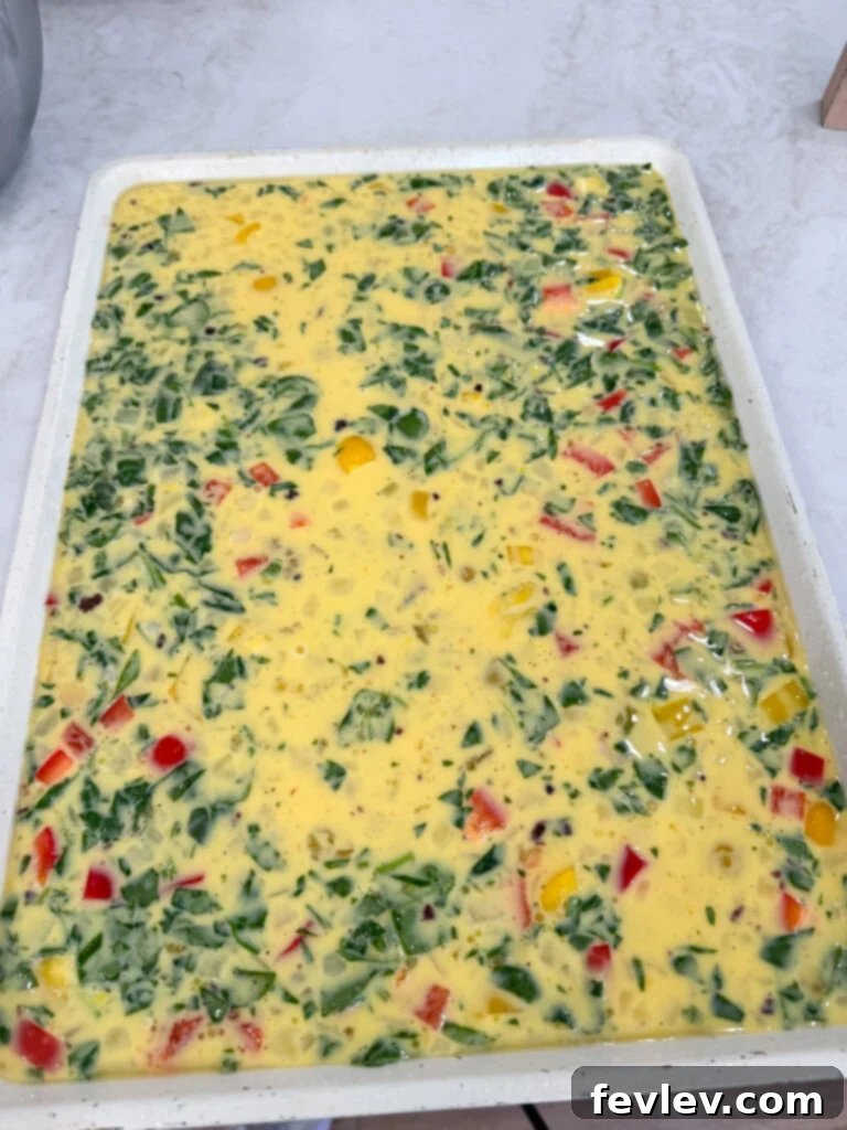 Make Ahead Sheet Pan Eggs for Breakfast Sandwiches 4 Egg mixture poured onto a sheet pan with meat