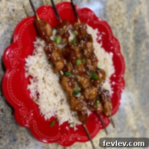 Delicious Teriyaki Chicken Skewers garnished with sesame seeds and green onions on a bed of rice.