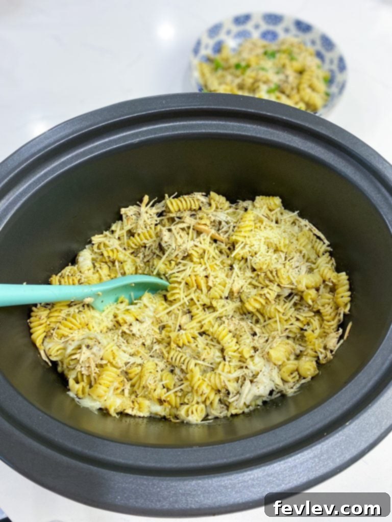 Creamy Slow Cooker Pesto Chicken Pasta 2 A close-up shot of Slow Cooker Pesto Chicken Pasta, showcasing tender chicken pieces, green pesto sauce, and melted cheese mixed with pasta in a slow cooker.