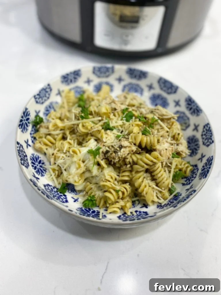 Creamy Slow Cooker Pesto Chicken Pasta 3 Ingredients laid out for Slow Cooker Pesto Chicken Pasta, including chicken breasts, jarred pesto, butter, various cheeses, and uncooked pasta.