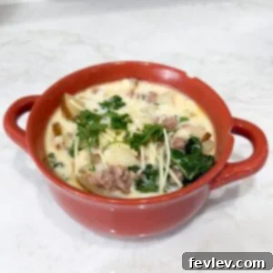 A beautiful bowl of creamy Slow Cooker Zuppa Toscana soup, generously topped with Parmesan cheese and a sprig of rosemary.