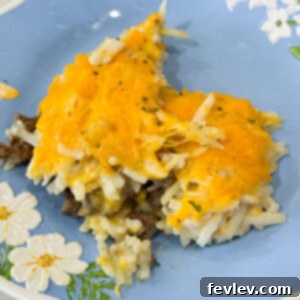 Baked hashbrown hamburger casserole on plate topped with melted cheese