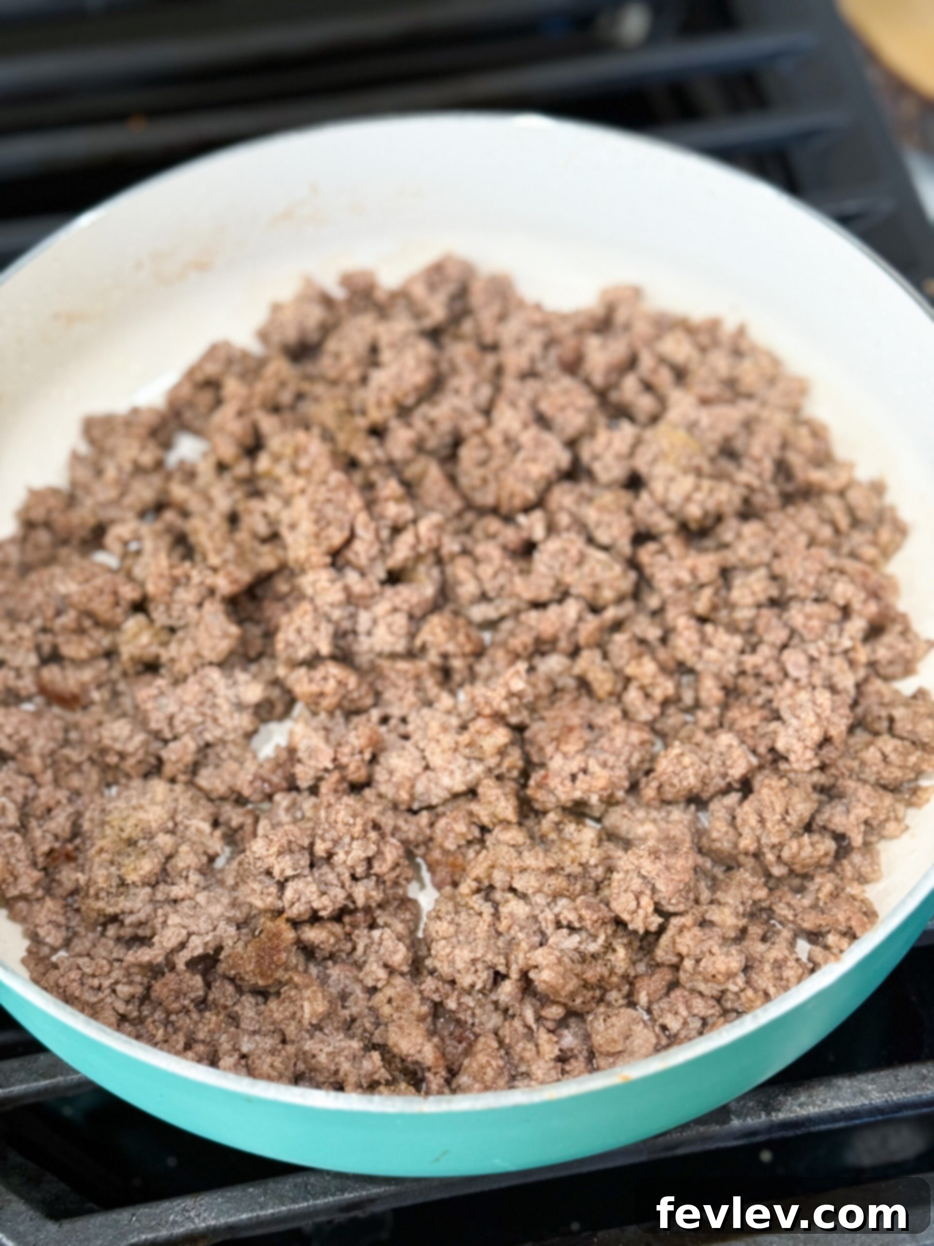 Golden Hashbrown Beef Bake 6 Ground beef cooking in a large skillet over medium heat, being broken apart with a wooden spoon.