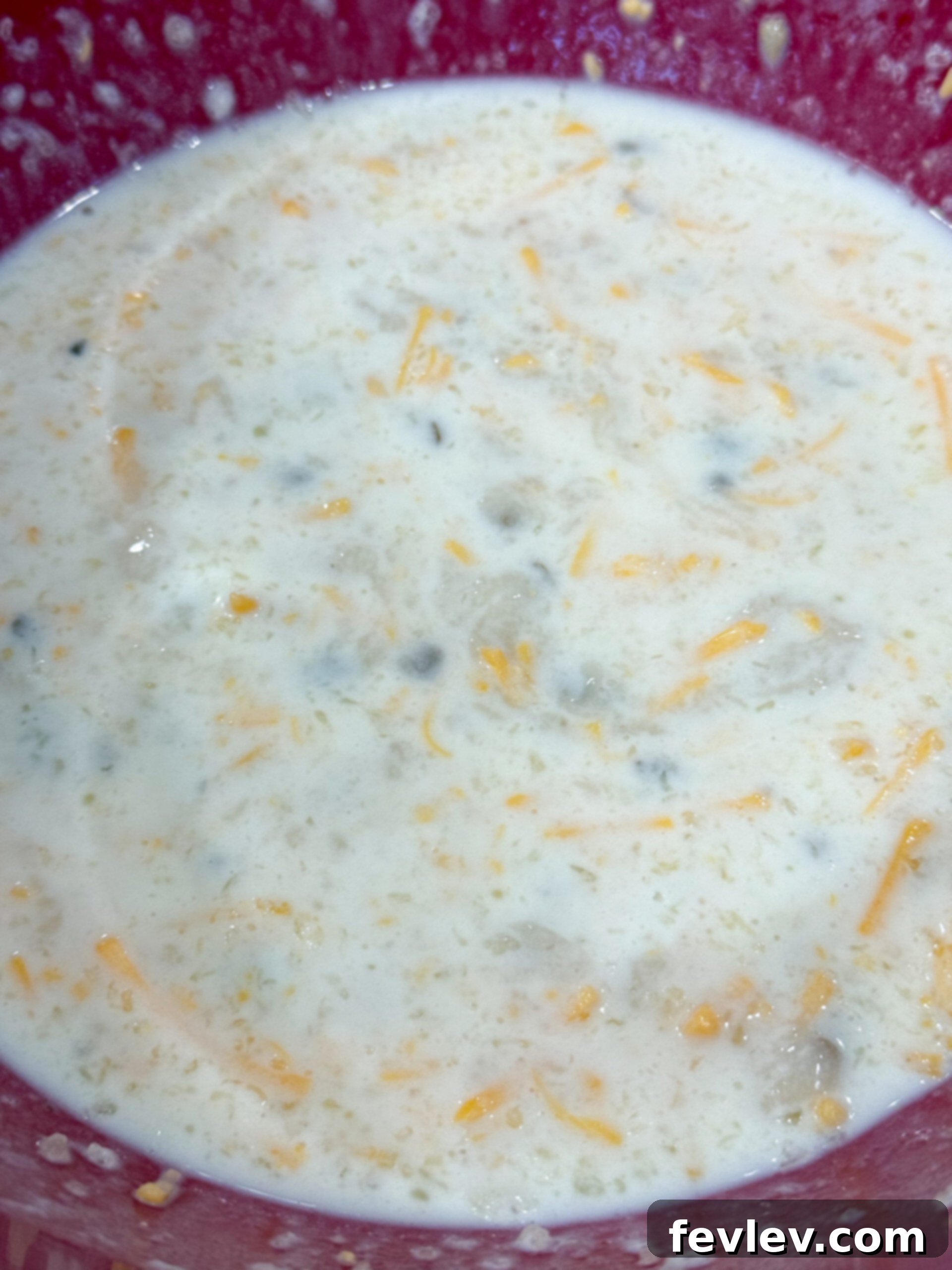 Golden Hashbrown Beef Bake 7 A large mixing bowl containing cream of mushroom soup, milk, and shredded cheese being whisked together until smooth and creamy.
