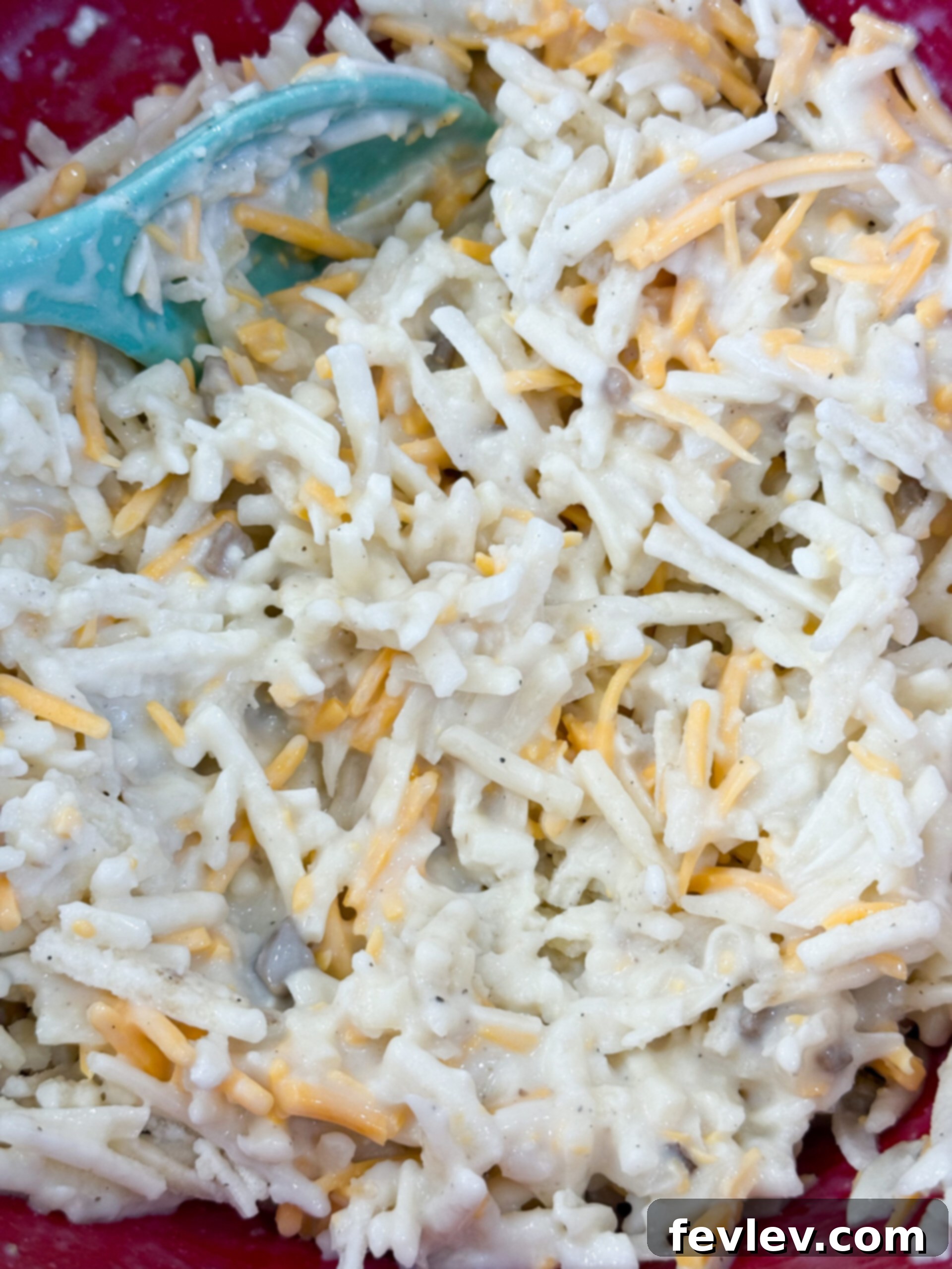 Golden Hashbrown Beef Bake 8 Shredded frozen hashbrowns being added to the creamy soup and cheese mixture in a large bowl, ready to be stirred.