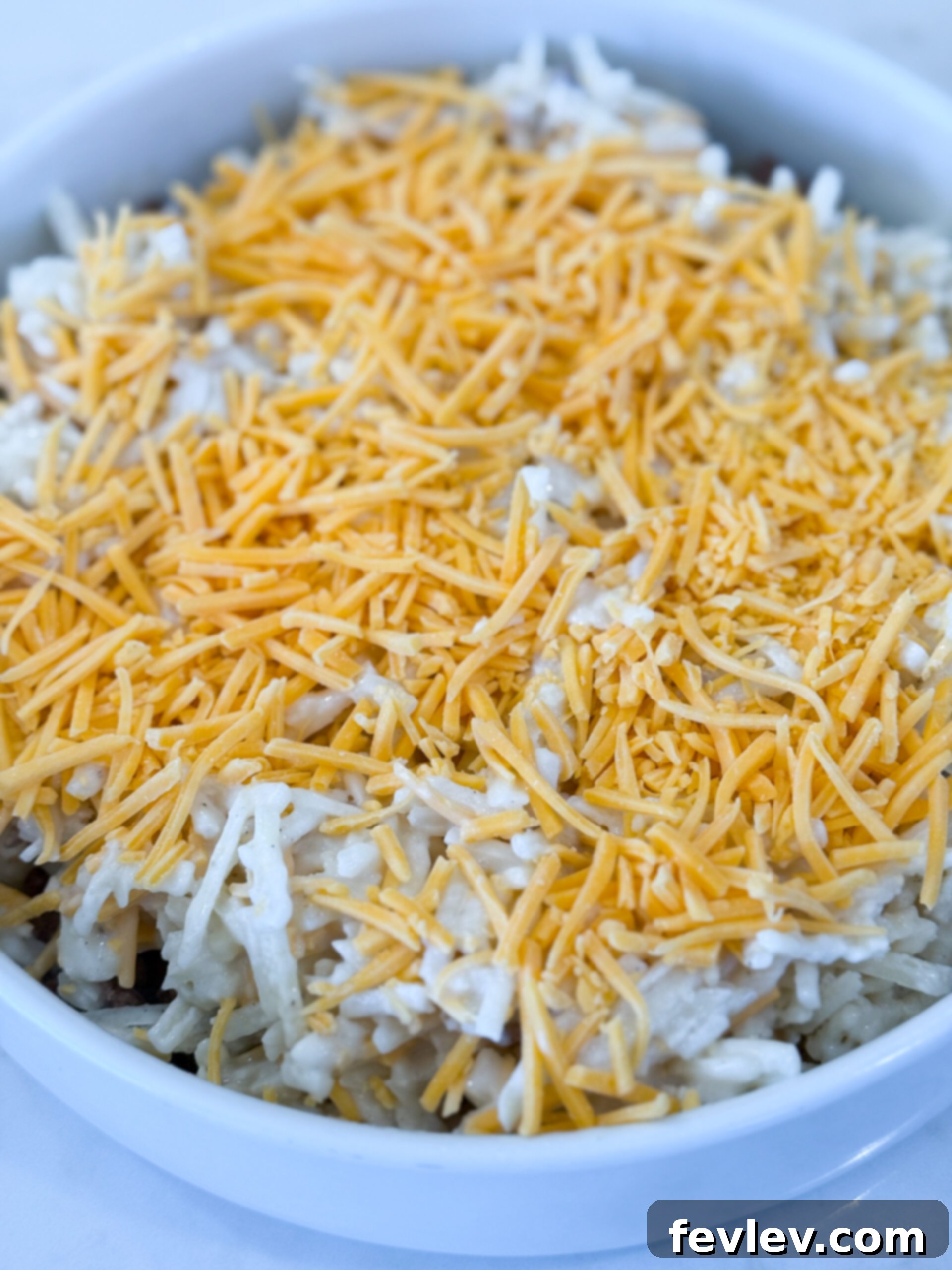 Golden Hashbrown Beef Bake 10 The hashbrown mixture being spread evenly over the layer of ground beef in the baking dish, before being topped with more cheese.