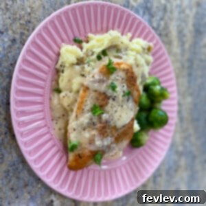 Golden brown chicken breasts drenched in a rich, creamy garlic sauce, garnished with fresh herbs, ready to be served over mashed potatoes.