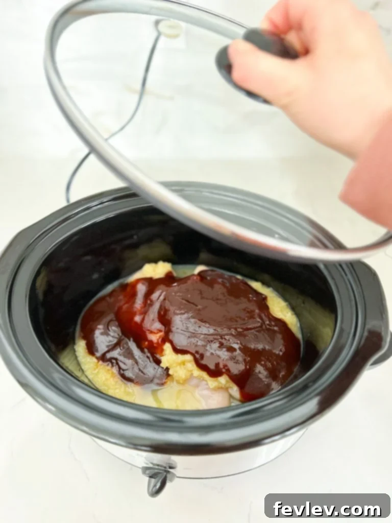 A selection of ingredients for Slow Cooker Pineapple Barbecue Chicken, including raw chicken breasts, a bottle of barbecue sauce, a can of pineapple chunks, a head of garlic, and a bottle of soy sauce.