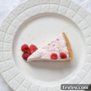 A slice of raspberry lemon no-bake cheesecake on a plate, garnished with fresh raspberries and lemon zest.