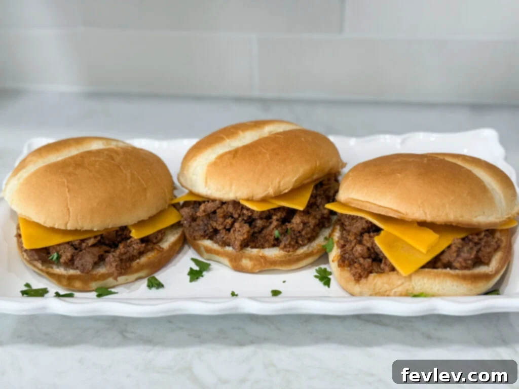Weeknight Sloppy Joe Winner 6 Simple Sloppy Joe sandwiches with cheese on hamburger buns on a long white plate on top of a white counter