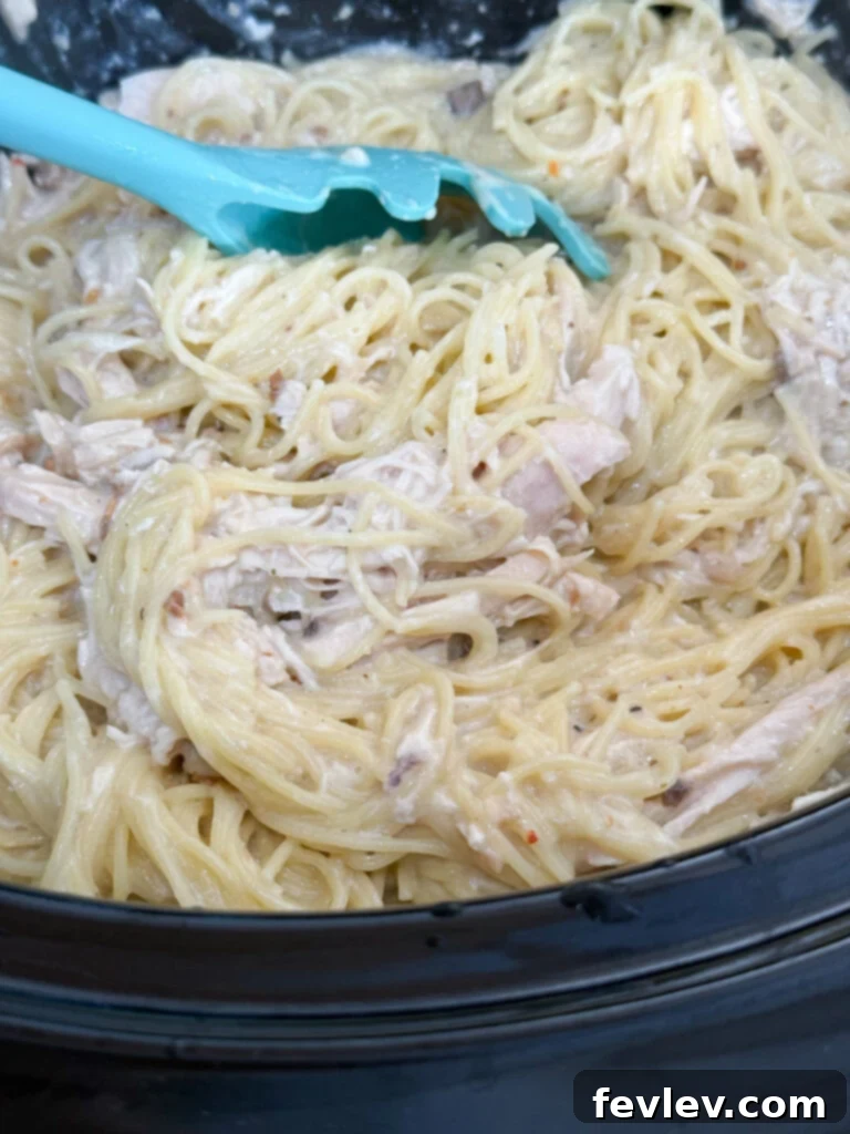 Cozy Slow Cooker Creamy Chicken Pasta 11 Adding cooked pasta to the creamy chicken mixture for a delicious meal