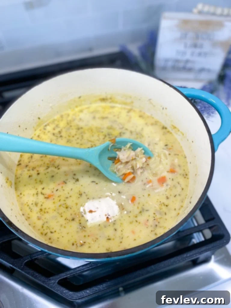 Close-up of creamy chicken orzo soup in a bowl with a spoon, showing tender chicken, orzo, and vegetables.