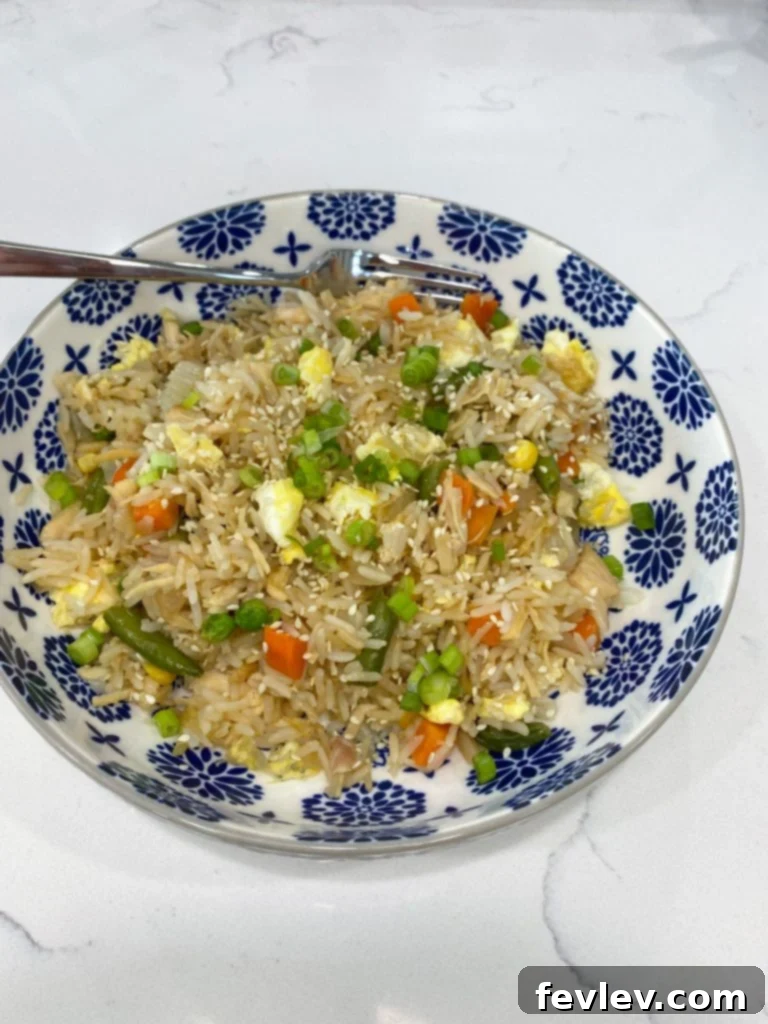 Close-up of freshly made Easy Chicken Fried Rice with chicken pieces, mixed vegetables, and scrambled egg, garnished with green onions.