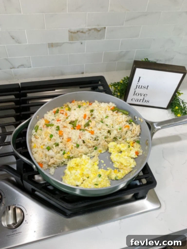 Chicken fried rice being stir-fried in a large skillet, showing ingredients like chicken, rice, and vegetables mixing together.