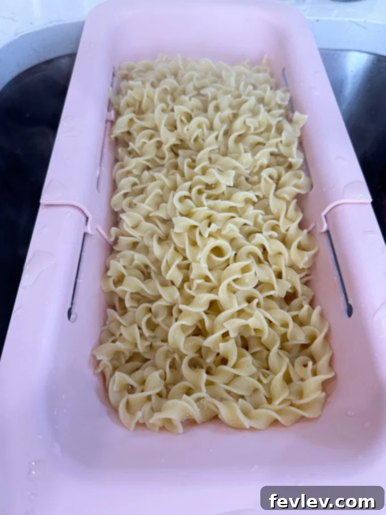 Egg noodles being freshly drained in a colander after boiling.
