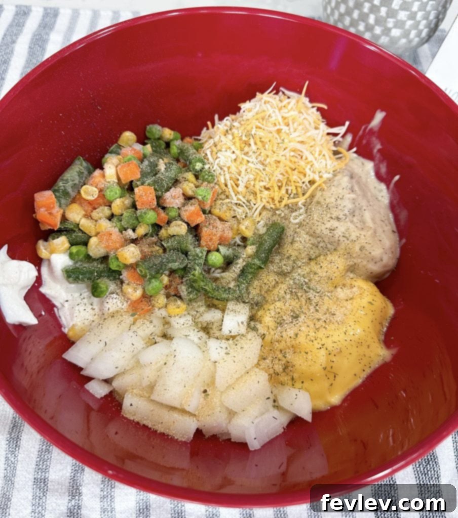 A large mixing bowl containing creamy casserole ingredients, including chicken, soups, and vegetables, being stirred together.