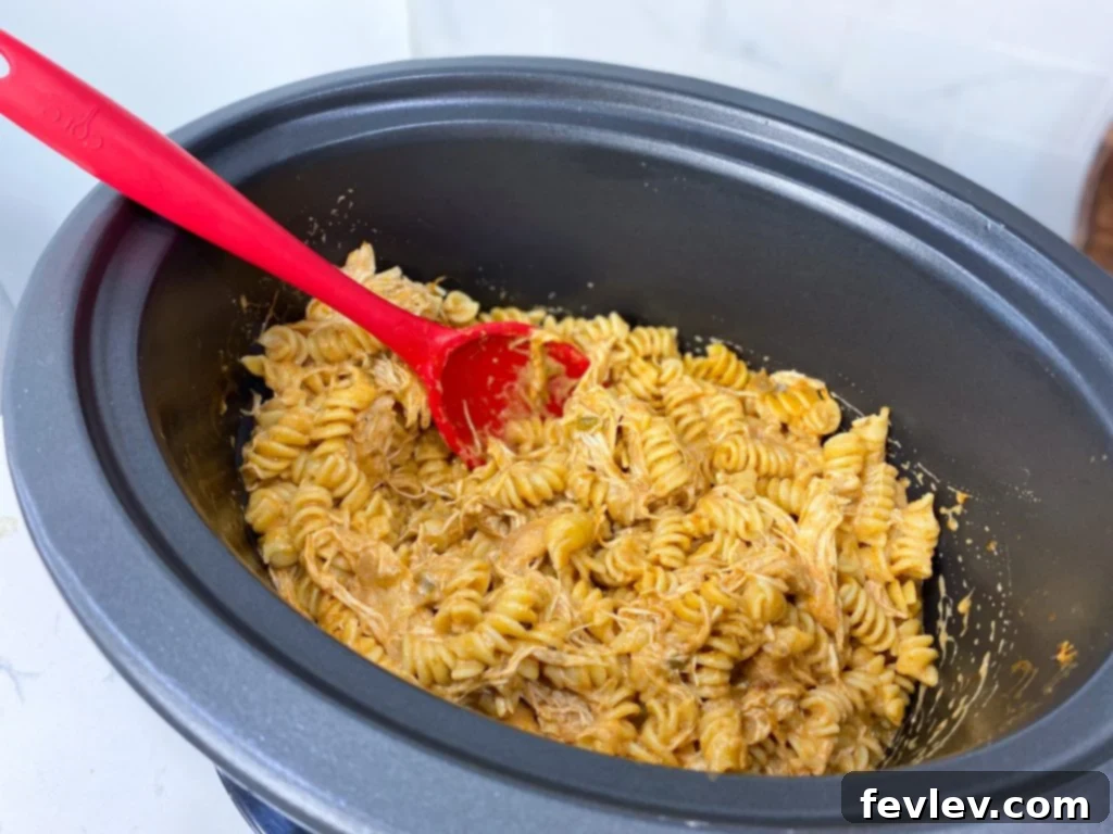Close-up of shredded chicken and pasta mixed with creamy enchilada sauce in a slow cooker.