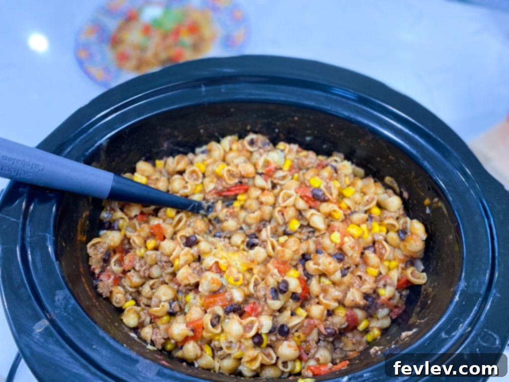 Slow Cooker Fiesta Pasta 4 Close-up of a serving of Slow Cooker Mexican Pasta in a bowl, garnished with sour cream, cilantro, and diced tomatoes