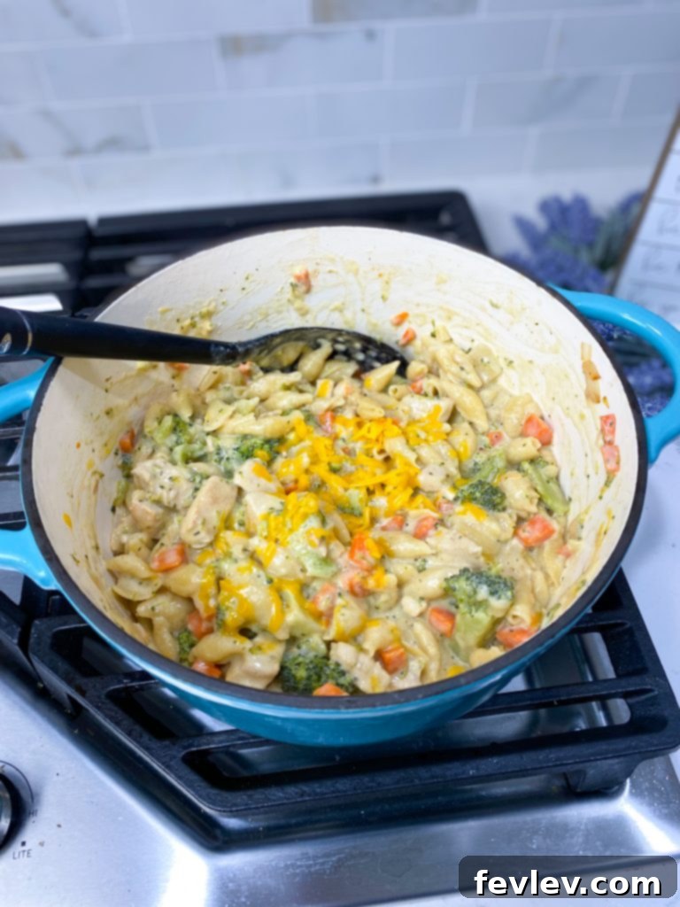 Close-up of raw ingredients for Cheesy Chicken and Broccoli Pasta, including chopped broccoli, carrots, onions, cubed chicken, and various spices arranged on a rustic wooden board.