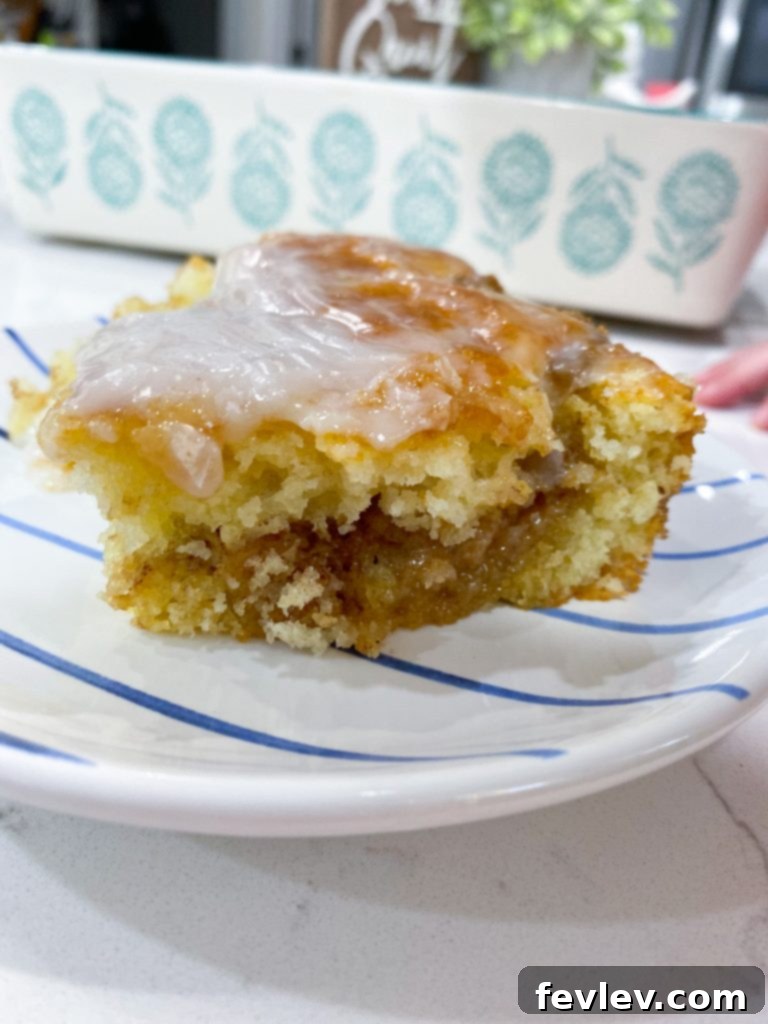 Close-up of a slice of Honey Bun Cake showing moist layers and cinnamon swirl with glaze.