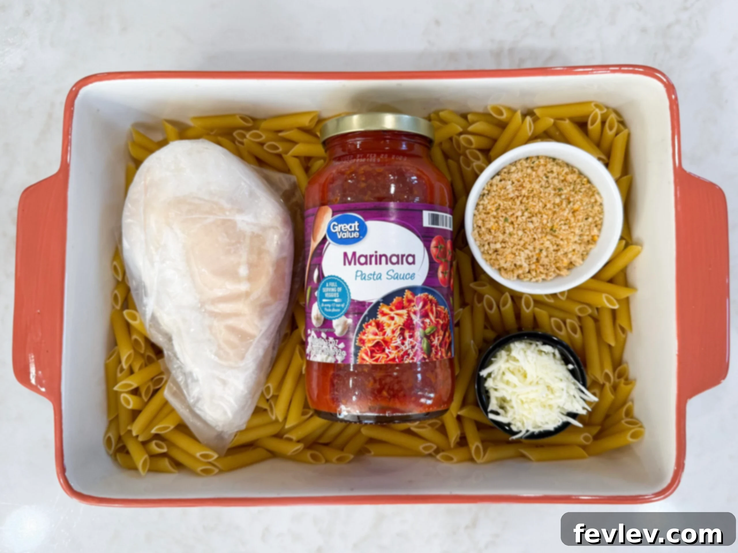 A vibrant display of fresh ingredients for chicken parmesan casserole, including chicken, pasta, marinara, and cheeses, arranged in a casserole dish before baking