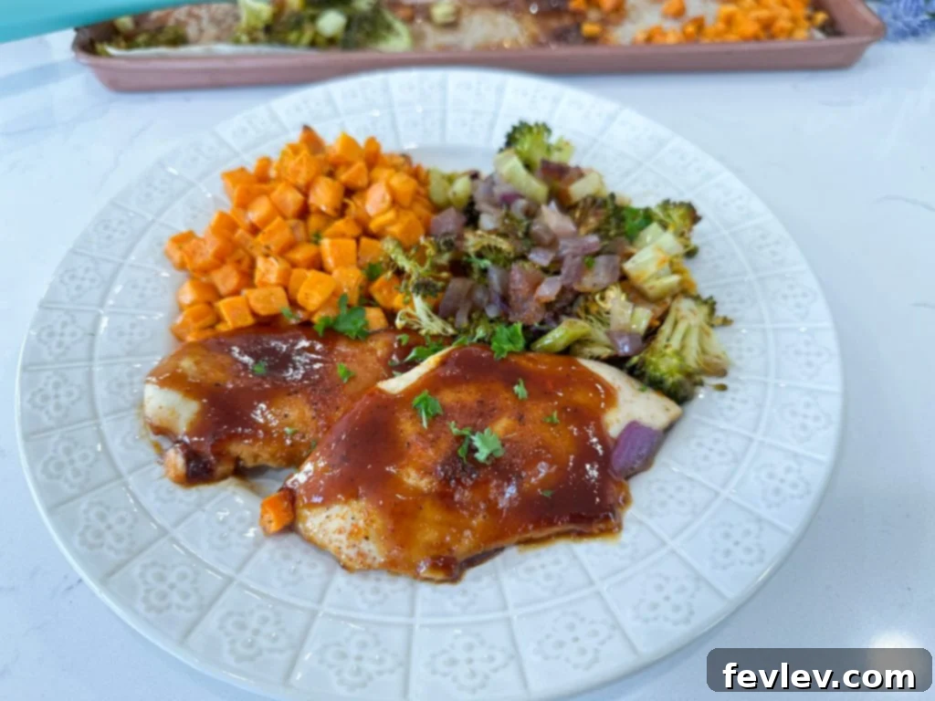 A completed sheet pan BBQ chicken and vegetables dinner, garnished with fresh herbs, ready to be served.