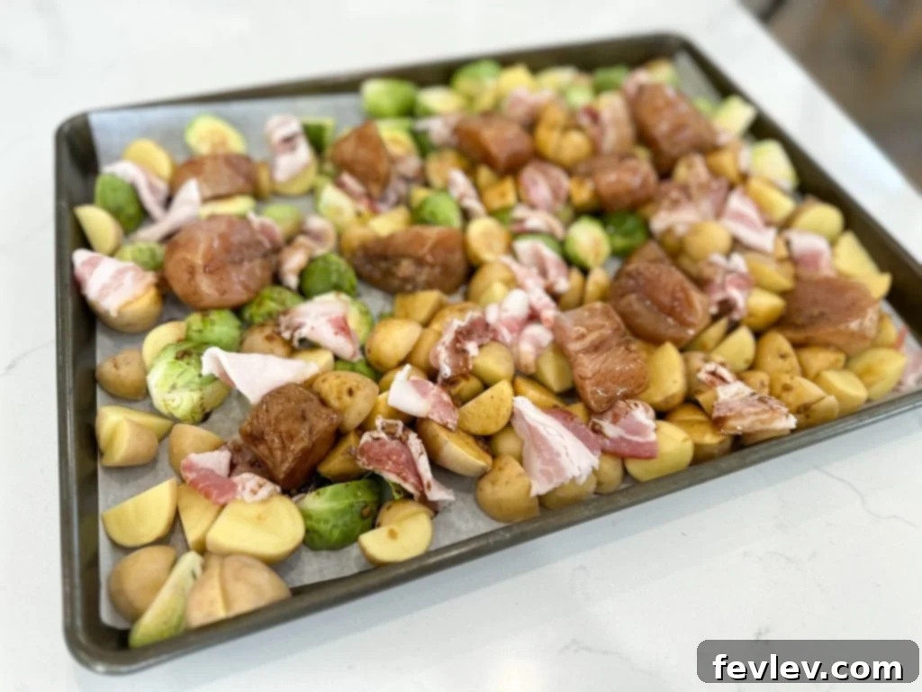 Close-up of marinated chicken, halved Brussels sprouts, and chopped golden potatoes on a baking sheet before roasting