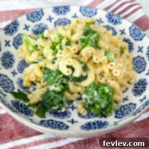 A bowl of creamy White Mac and Cheese with broccoli florets, garnished and ready to serve.