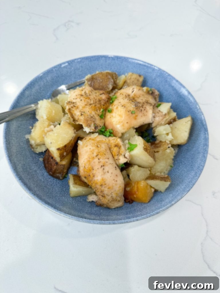 Cooked garlic butter chicken thighs and potatoes served in a bowl, garnished with fresh herbs.