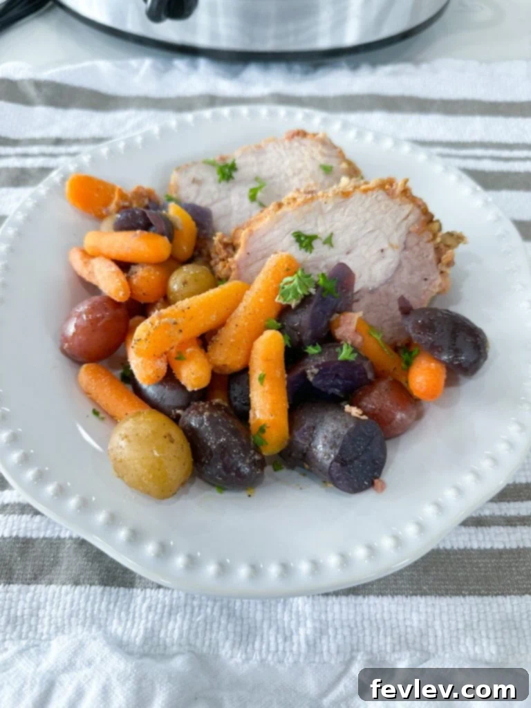 Melt-in-Your-Mouth Slow Cooker Pork Tenderloin 6 A complete meal of slow cooker pork tenderloin, potatoes, and carrots, served with a side of warm dinner rolls on a wooden table.